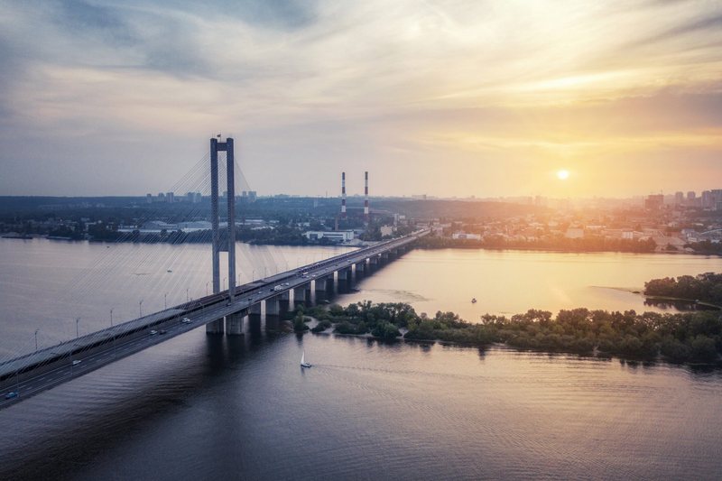 A cable-stayed bridge crossing a wide river at sunset, photographed from the air.